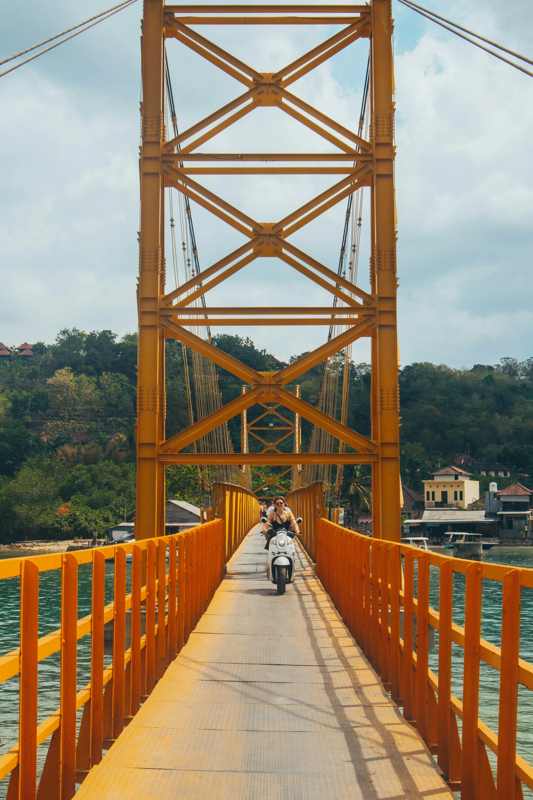 A rider crossing the yellow suspension bridge between Ceningan and Lembongan